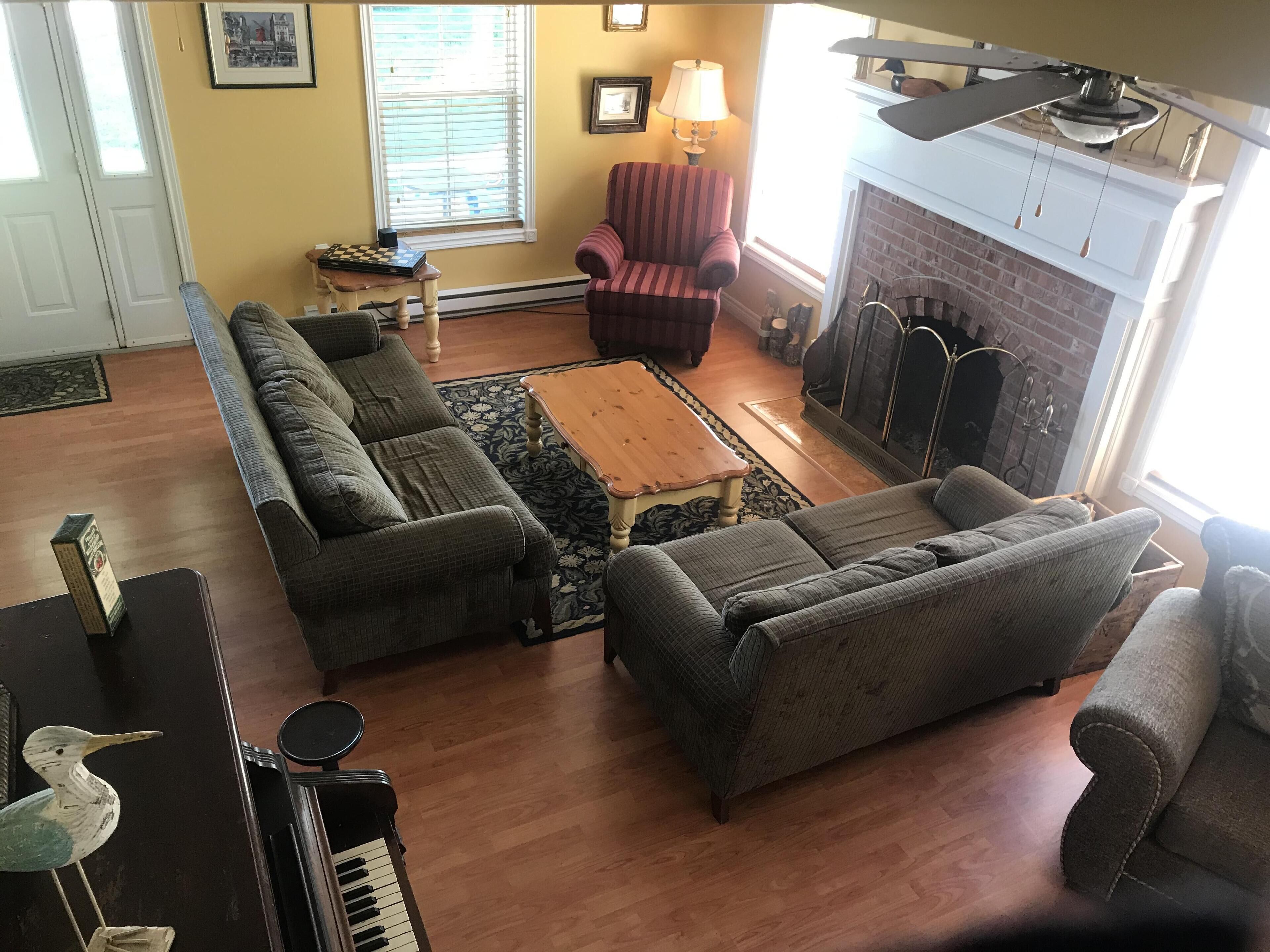 A living room with a sectional sofa, a small wooden coffee table, a fireplace, and a piano.