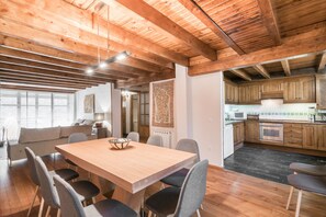 A spacious dining area with a wooden table and chairs, a kitchen with wooden cabinets, and a view of the adjacent living room.