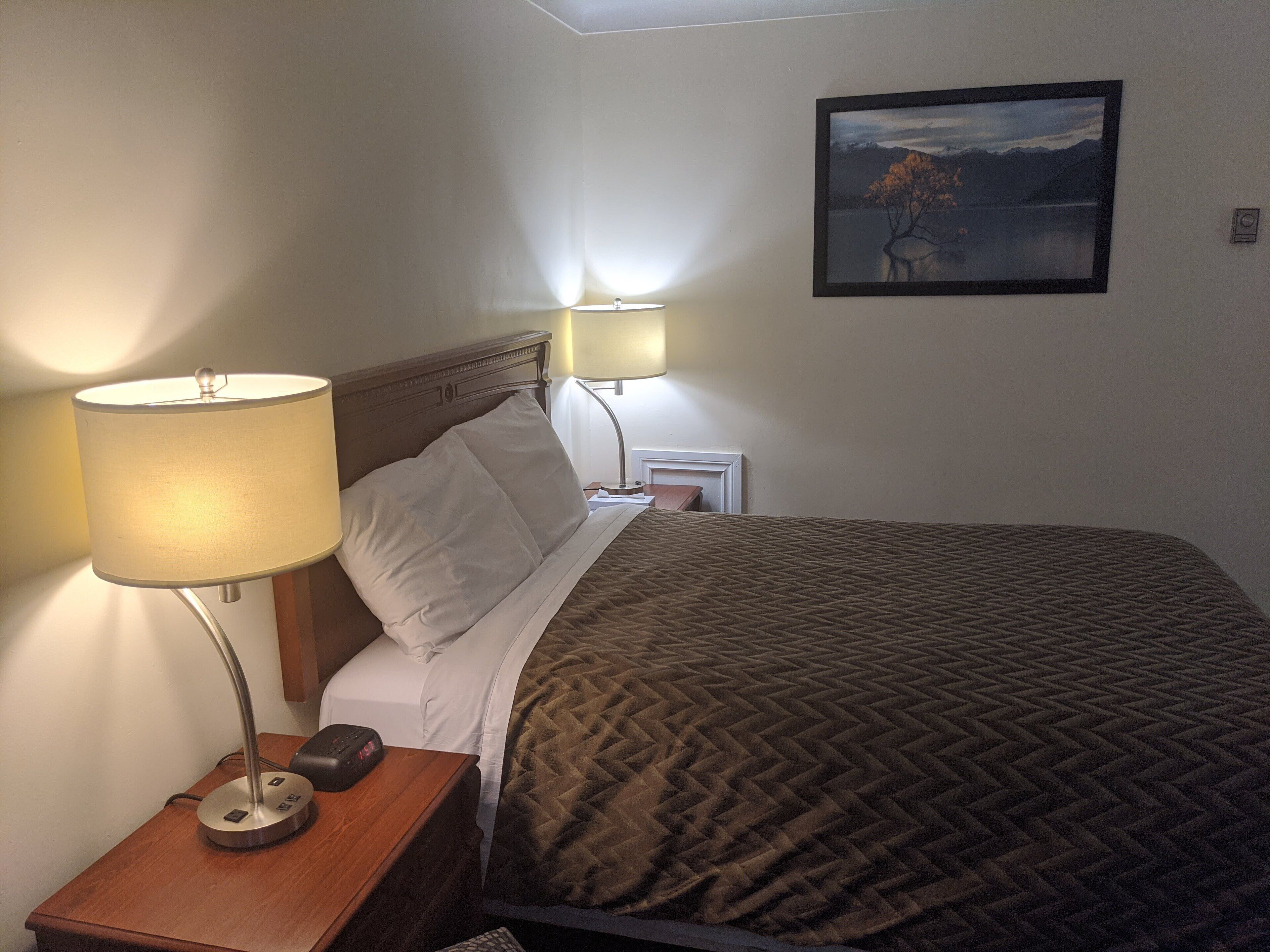A neatly made bed with a brown quilt, two bedside lamps, and a framed picture on the wall.