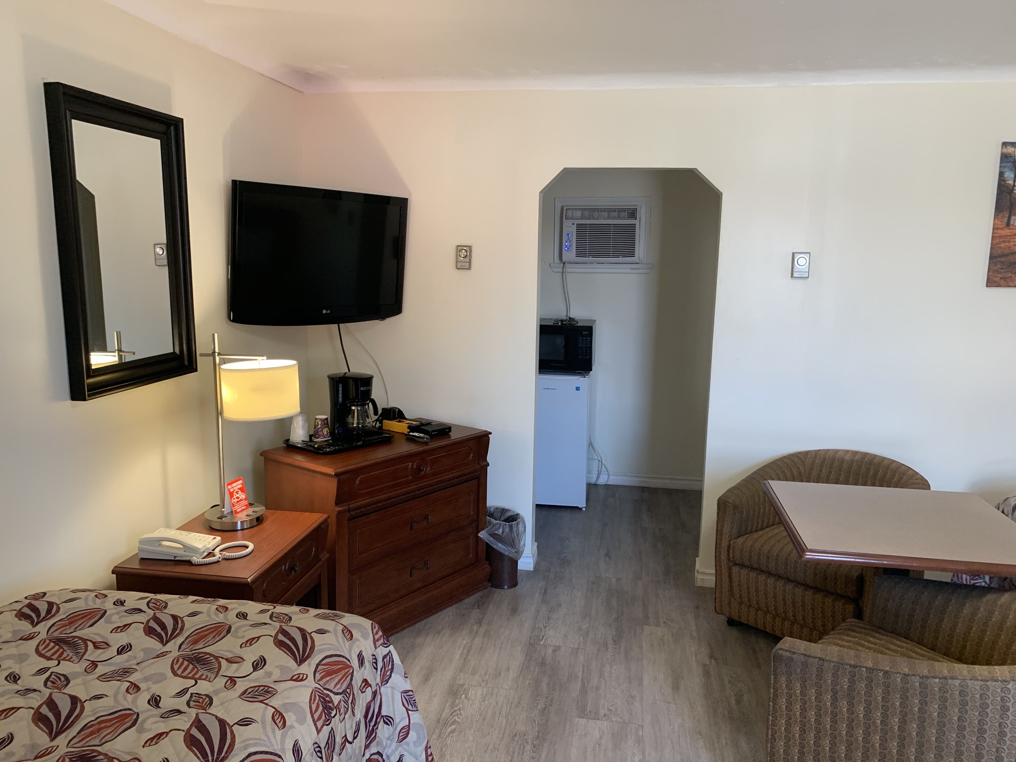 A hotel room with a bed, a desk, a chair, a television, a coffee maker, a microwave, and a small kitchenette.