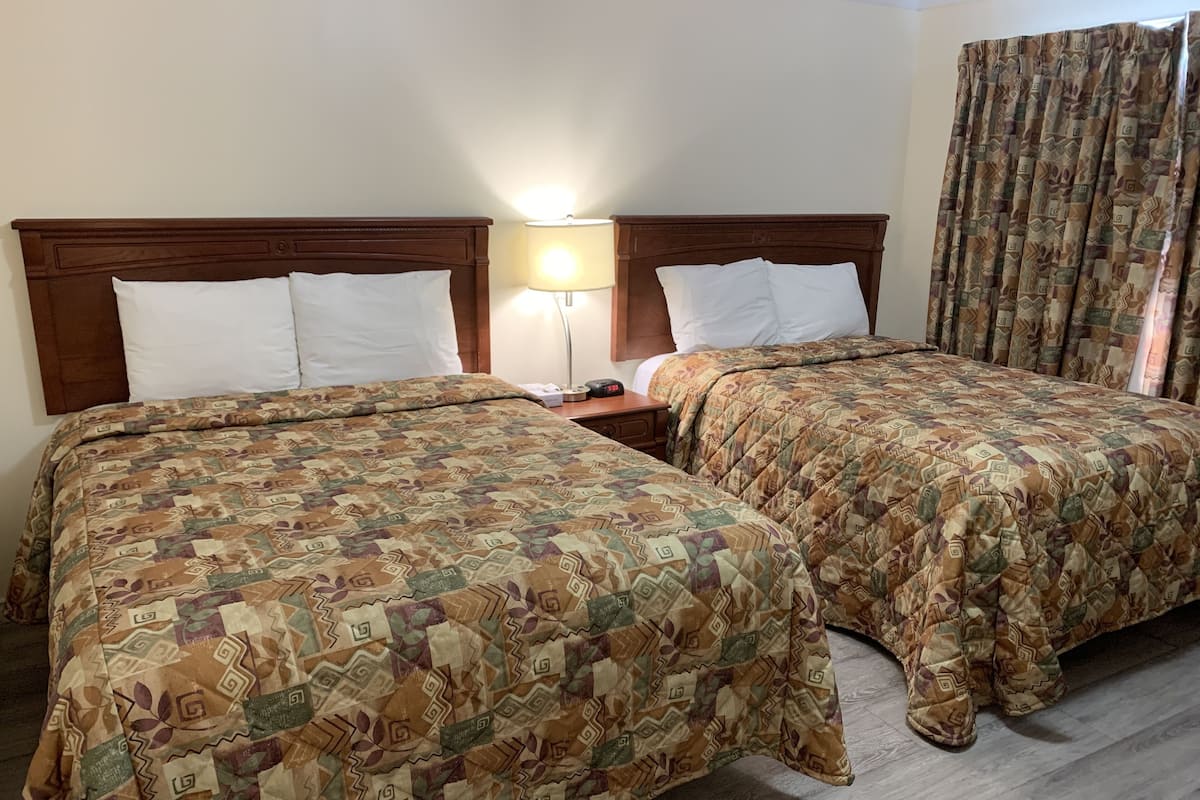 A hotel room with two beds, each with patterned bedding, a nightstand with a lamp, and a window with curtains.