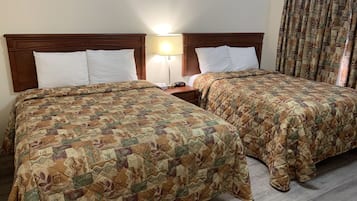 A hotel room with two beds, each with patterned bedding, a nightstand with a lamp, and a window with curtains.