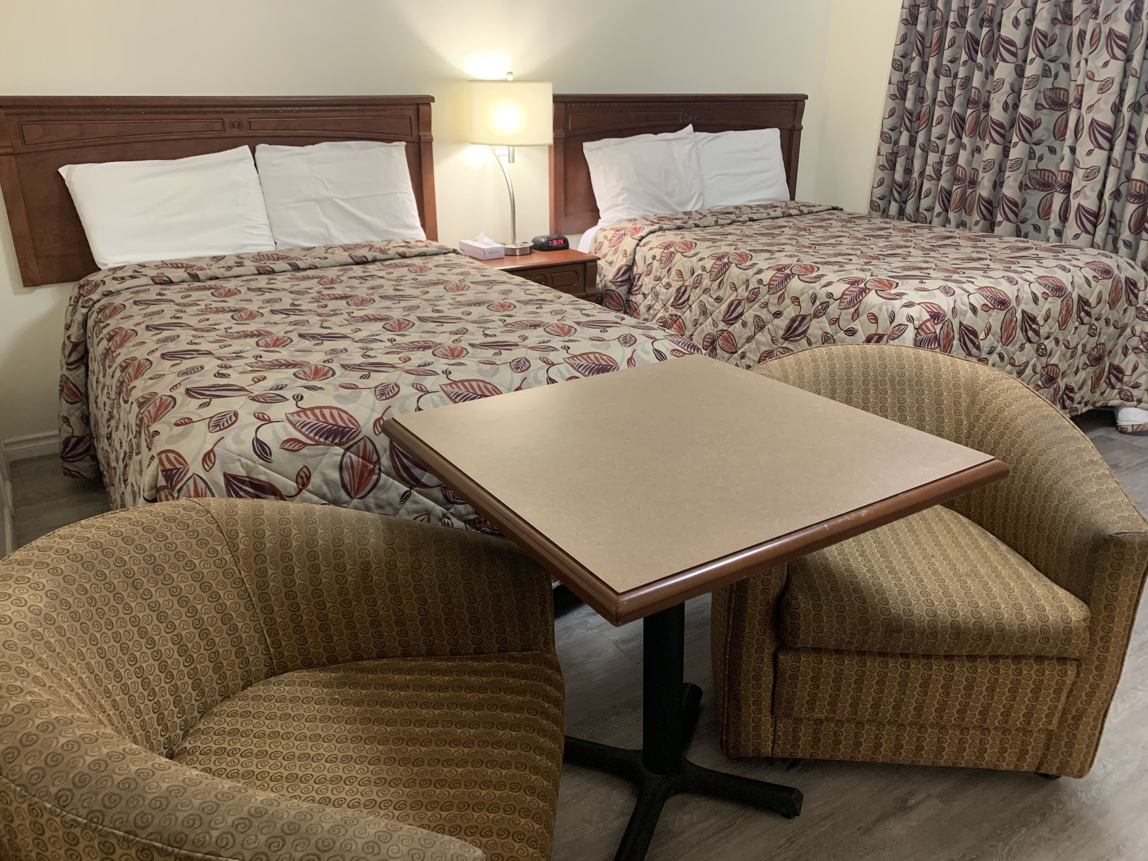 Een hotelkamer met twee bedden, een klein tafeltje en twee gestreept fauteuils.