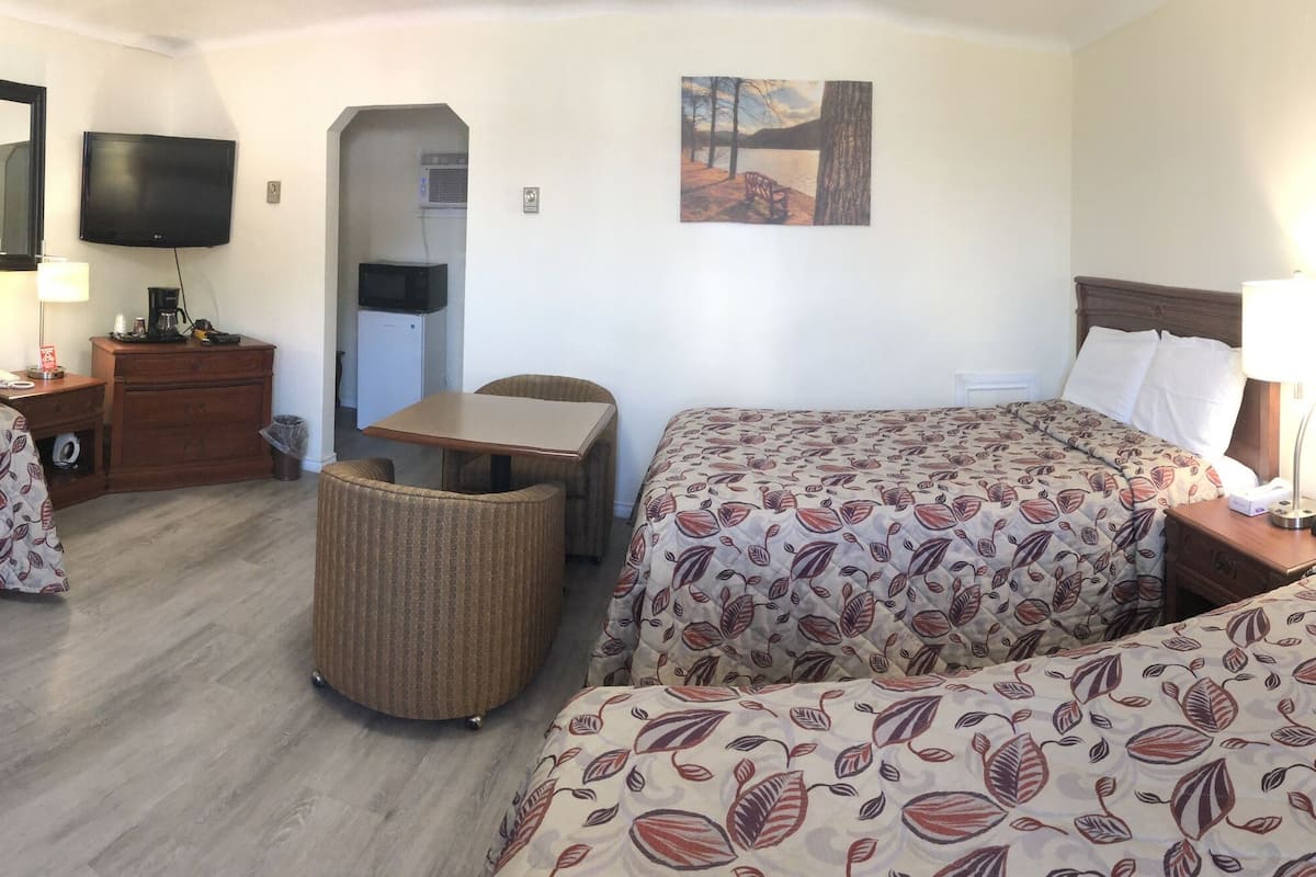 A hotel room with two beds, a TV, a small desk, a trash bin, and a painting on the wall.