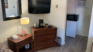 A hotel room with a wooden dresser, a flat-screen TV mounted on the wall, a coffee maker, a lamp, a telephone, and a trash can. - Century motel (Cornwall)