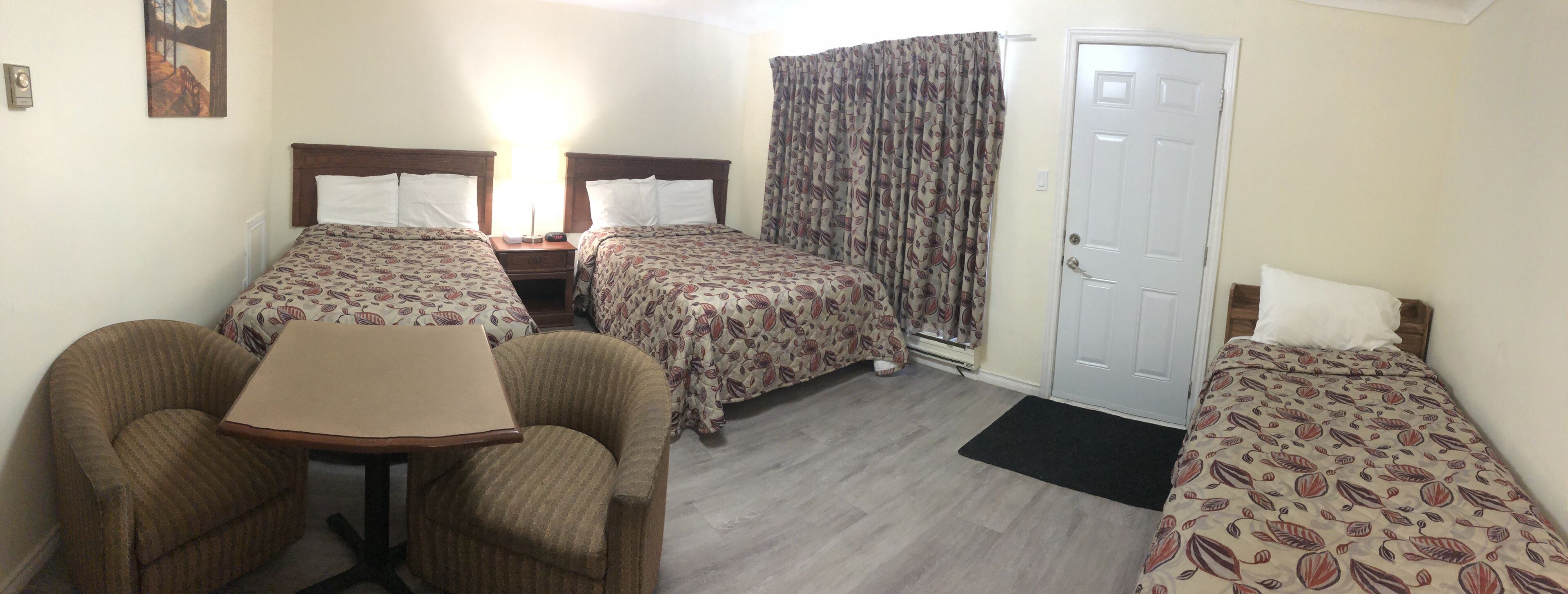 A hotel room with two single beds, a small table, two chairs, a door, and a window with curtains.