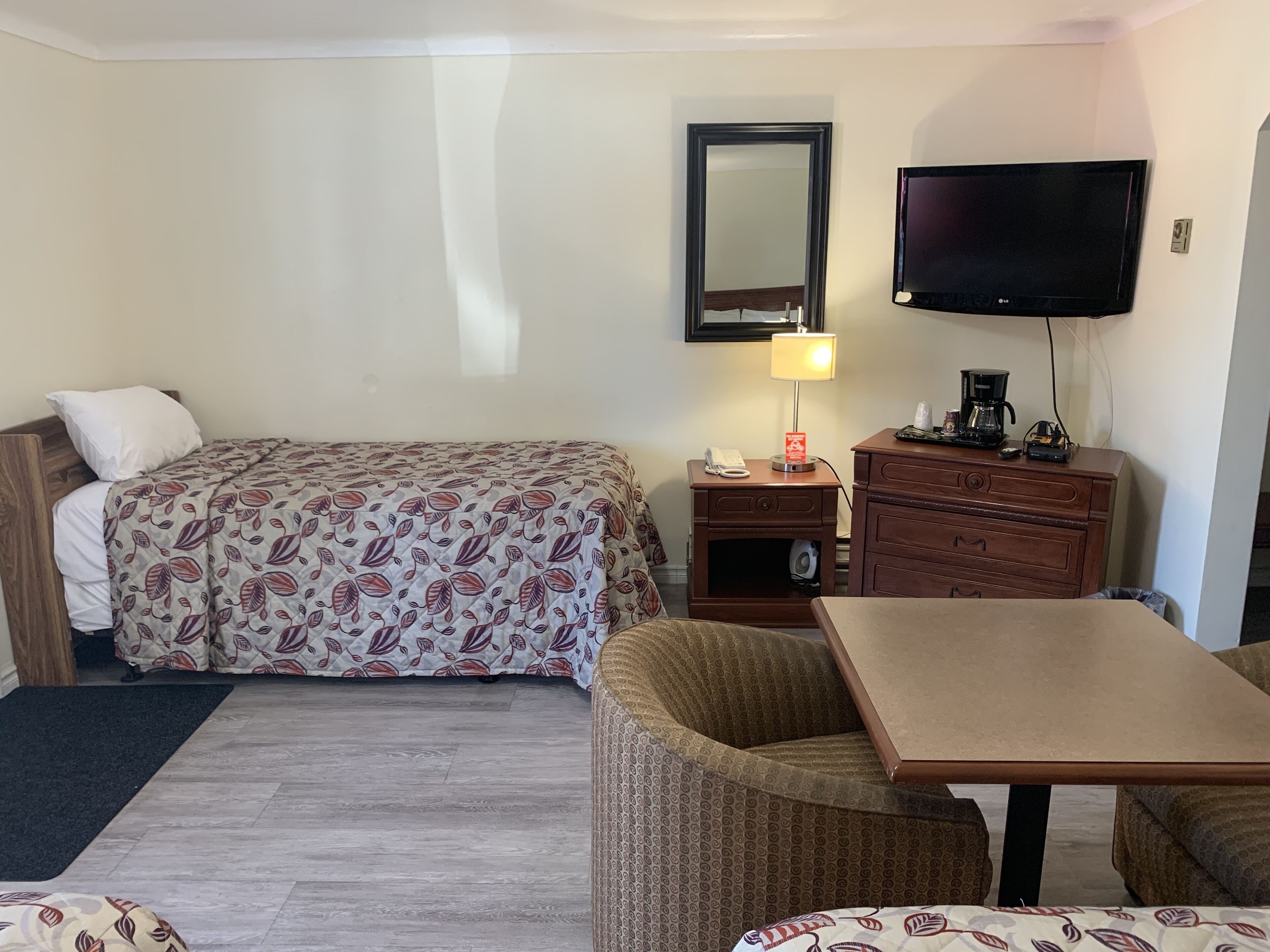 A hotel room with a bed, a desk, a chair, a television, and a dresser.