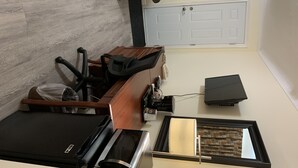 A compact hotel room with a kitchenette, a bed, a desk, and a window with a view of a patterned wall and a door. - Century motel (Cornwall)