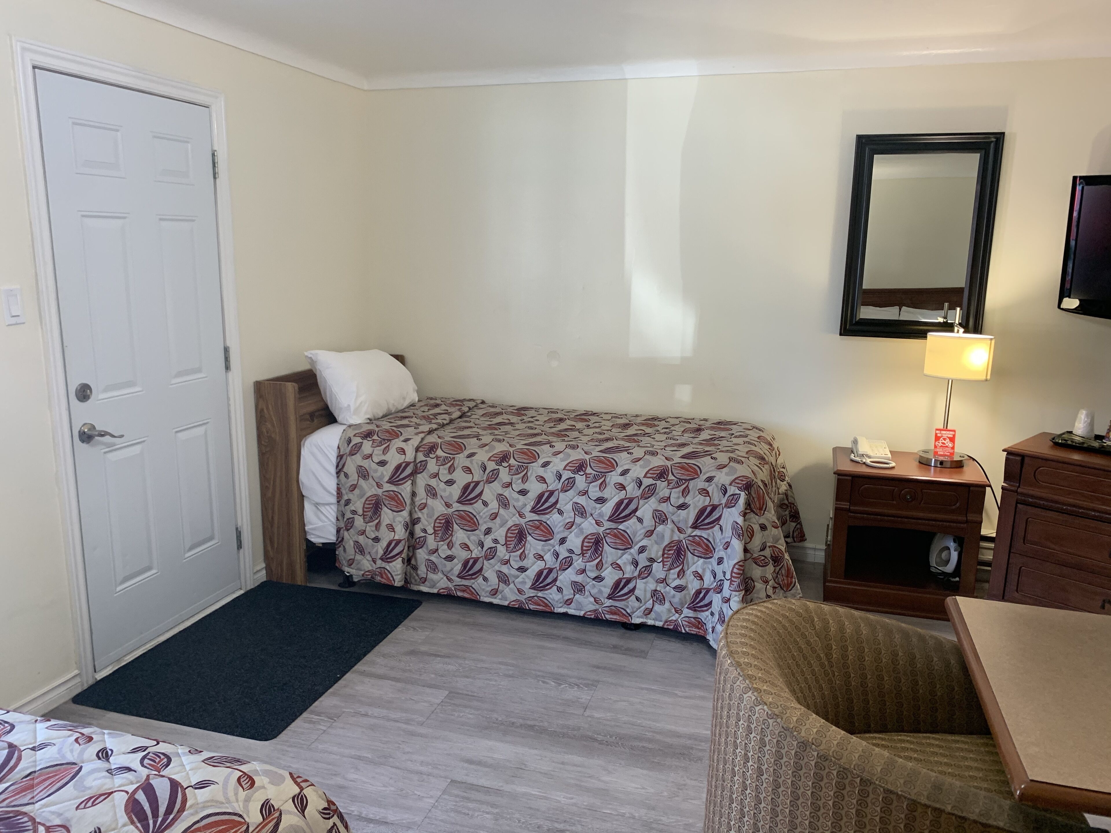 A hotel room with a bed, a desk, a chair, a desk lamp, a telephone, and a television.