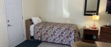 A hotel room with a bed, a desk, a chair, a desk lamp, a telephone, and a television.