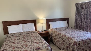 Habitación de hotel con dos camas, una mesita de noche con lámpara y una ventana con cortinas estampadas.