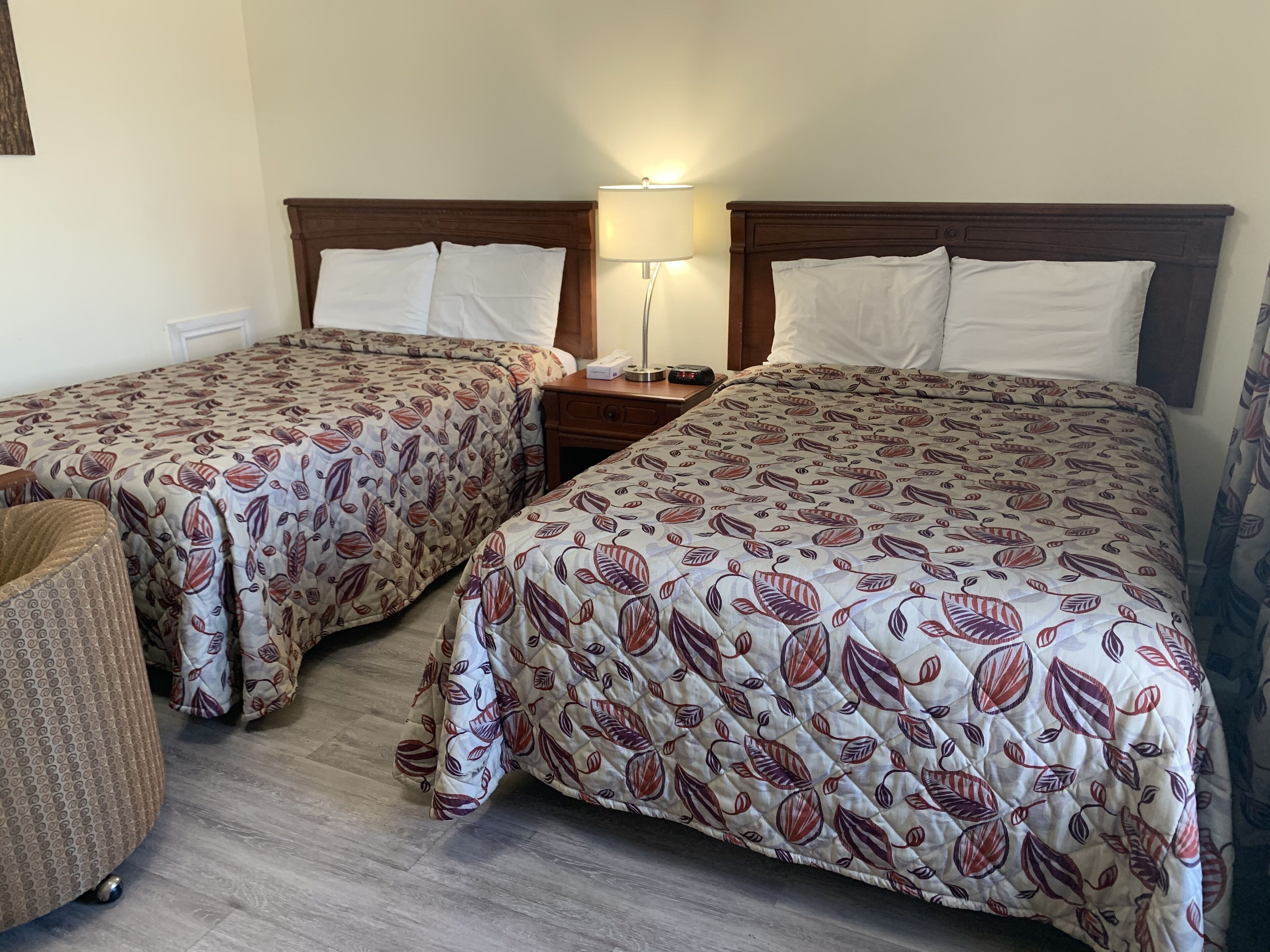 Dos camas individuales con ropa de cama estampada a flores, una mesita de noche con lámpara y una silla pequeña.