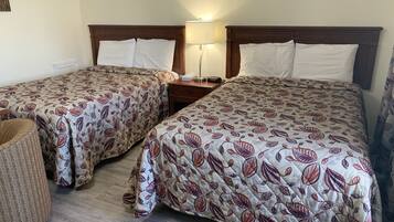 Dos camas individuales con ropa de cama estampada a flores, una mesita de noche con lámpara y una silla pequeña.