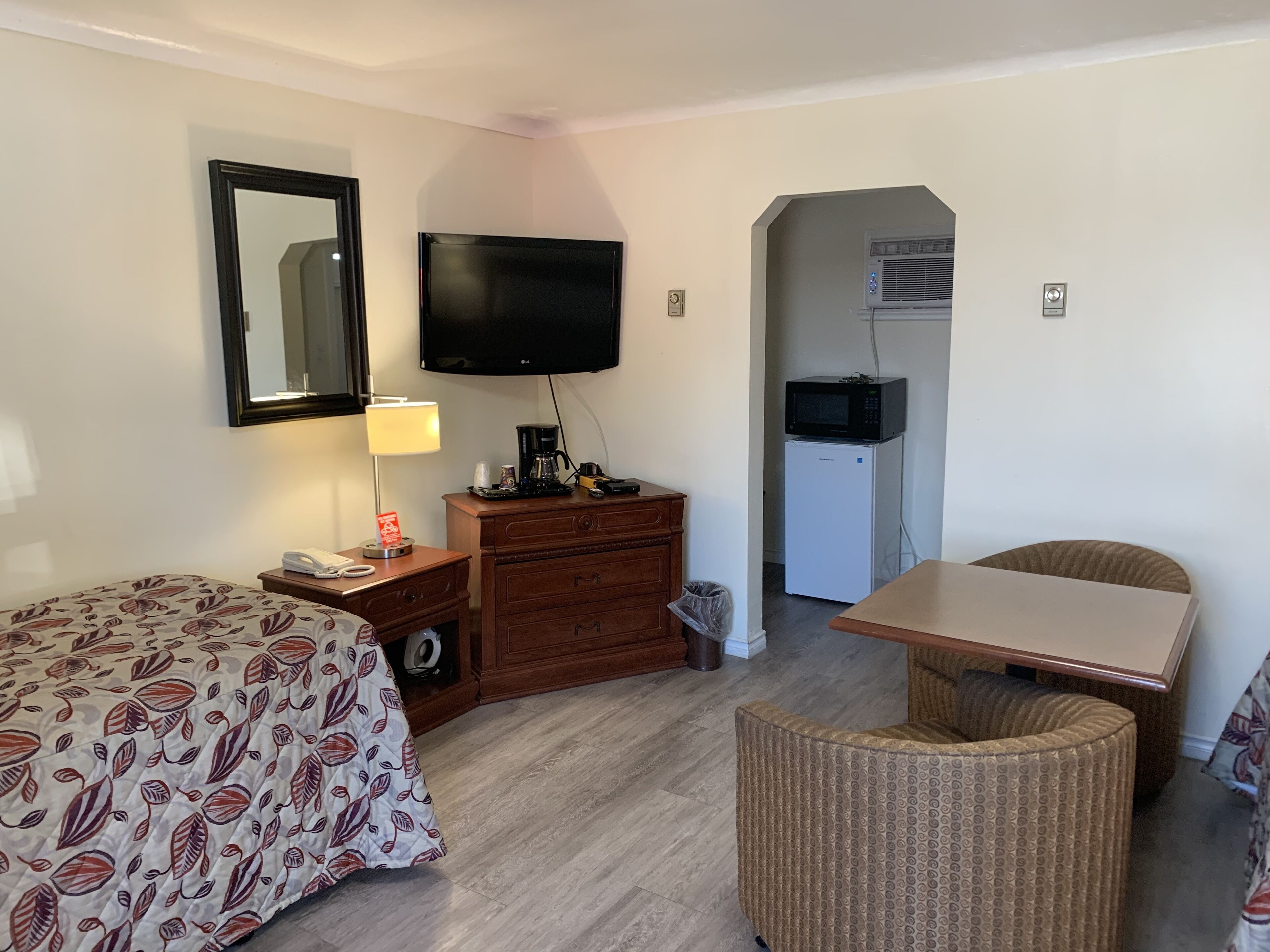 Une chambre d’hôtel équipée d’un lit, d’un bureau, d’une chaise, d’une commode, d’une télévision et d’un four à micro-ondes.