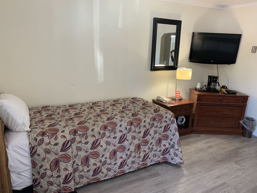 Una habitación de hotel con una cama, una mesita de noche, un aparador, un televisor y una lámpara.