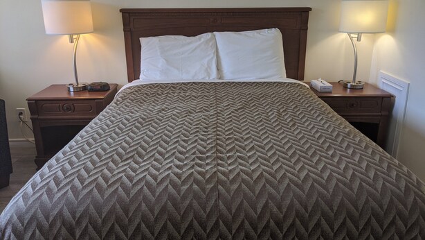 A neatly made bed with a patterned bedspread, two bedside lamps, and a nightstand with a clock and a phone. - Century motel (Cornwall)