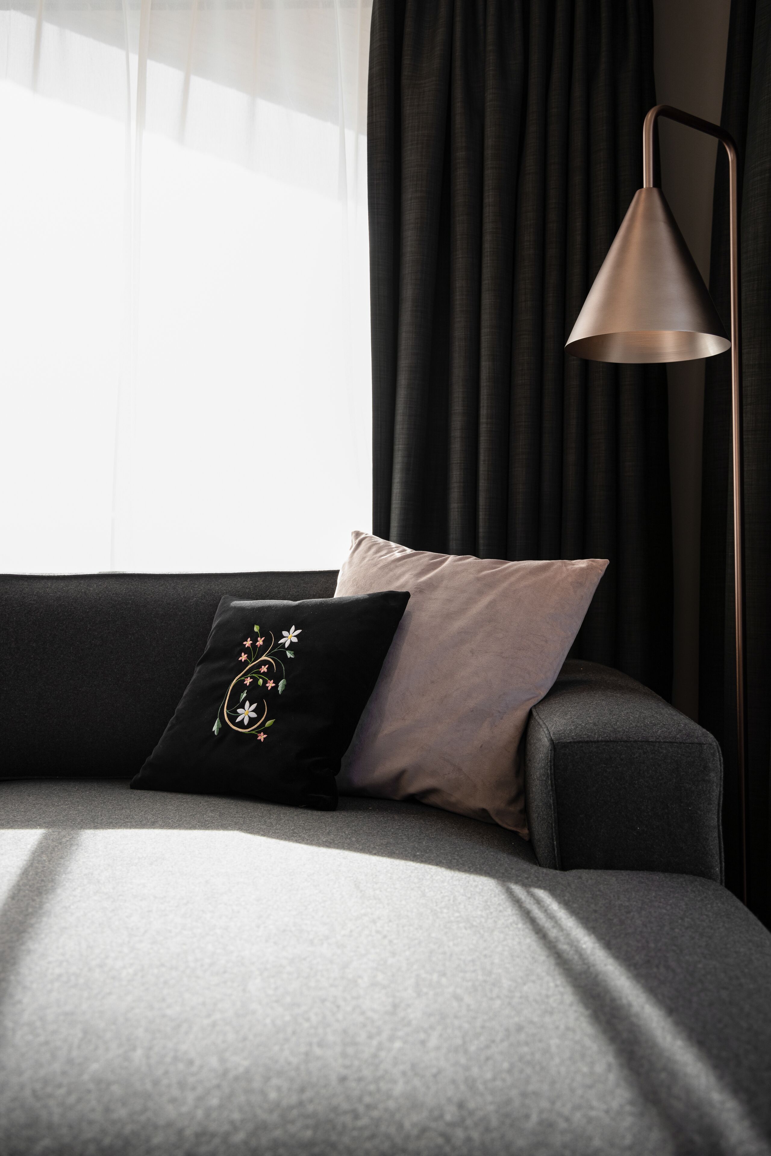 A modern living room with a sofa, a decorative pillow, a floor lamp, and a window with curtains.