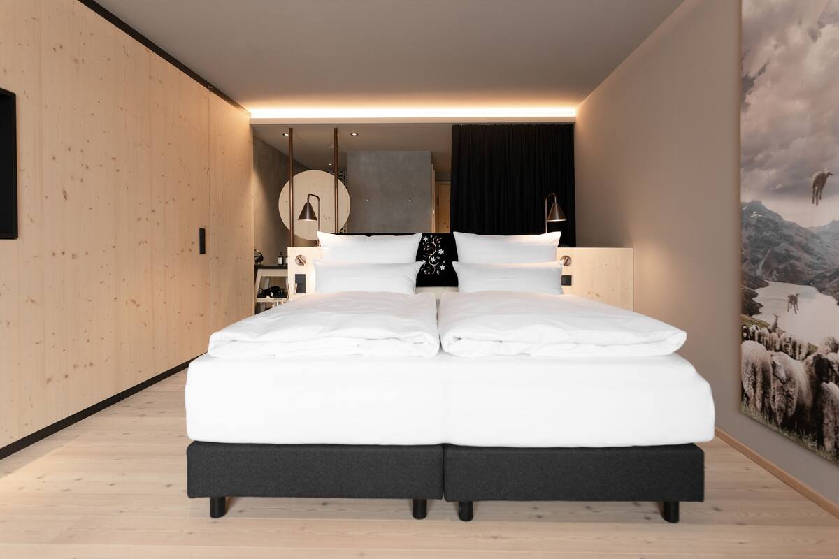 A modern bedroom with a large bed, wooden walls, a mounted artwork, and a nightstand with a lamp.