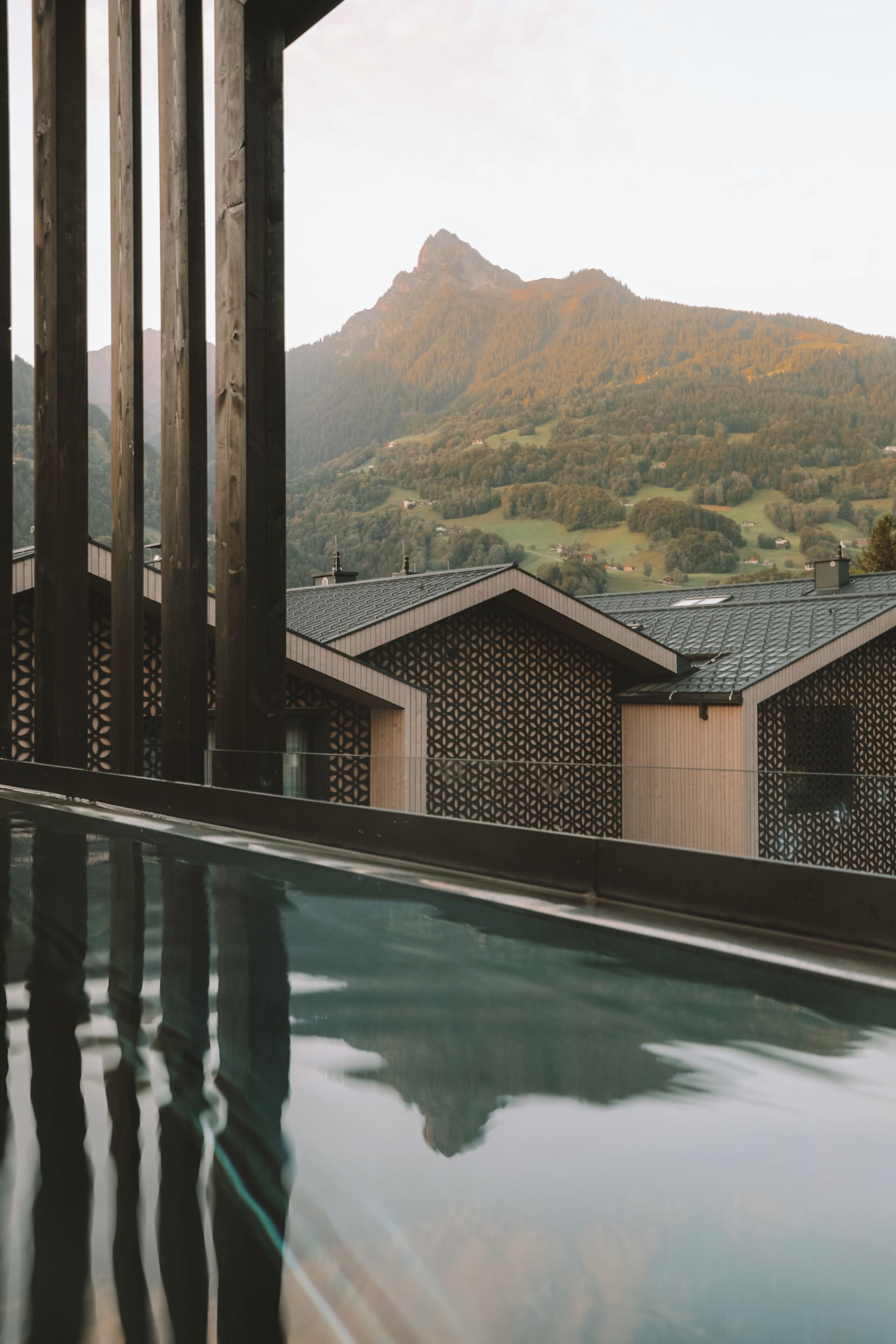 A modern building with a pool, wooden beams, and a mountain view.