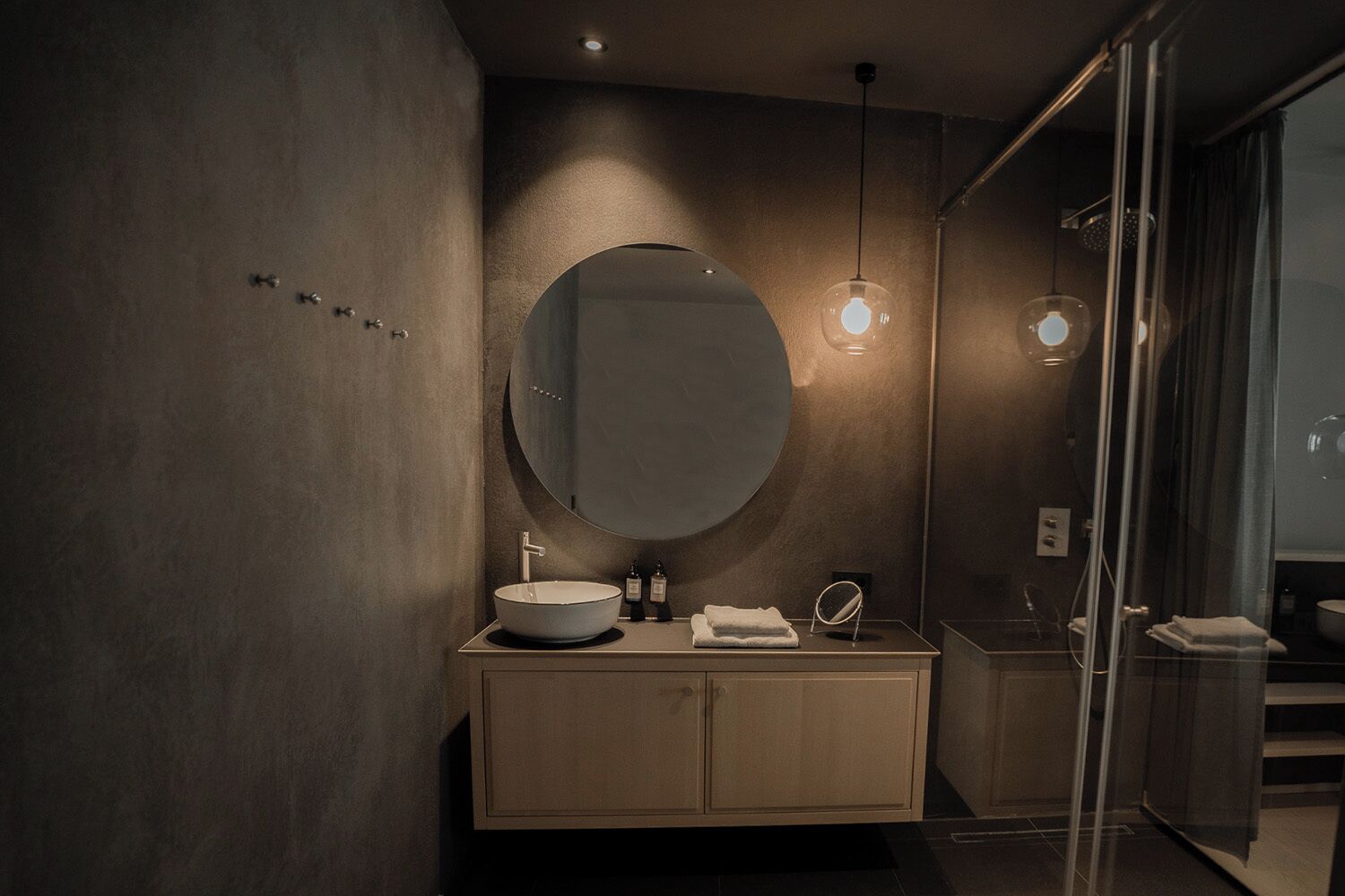 Un baño moderno con un espejo redondo, un lavamanos y una cabina de ducha de vidrio.