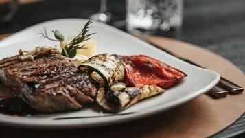A plate of food with a steak, vegetables, and a garnish on a table with a glass of red wine and a glass of water.
