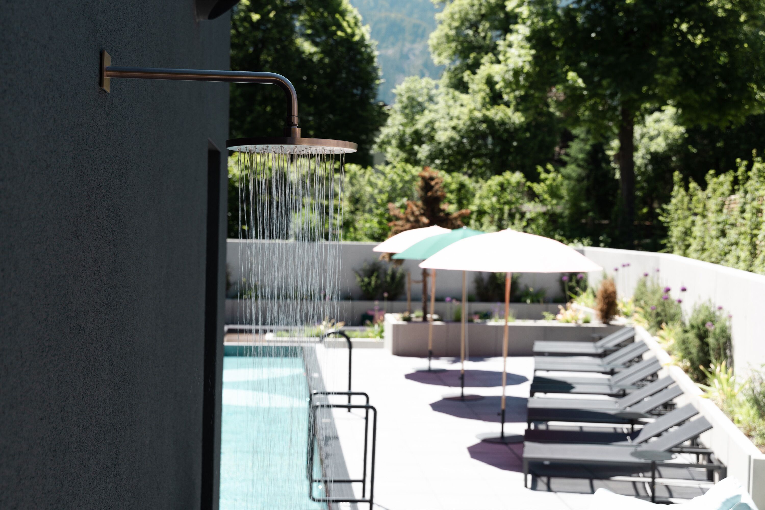 Ein Poolbereich mit Wasserspiel, Liegestühlen und Sonnenschirmen.