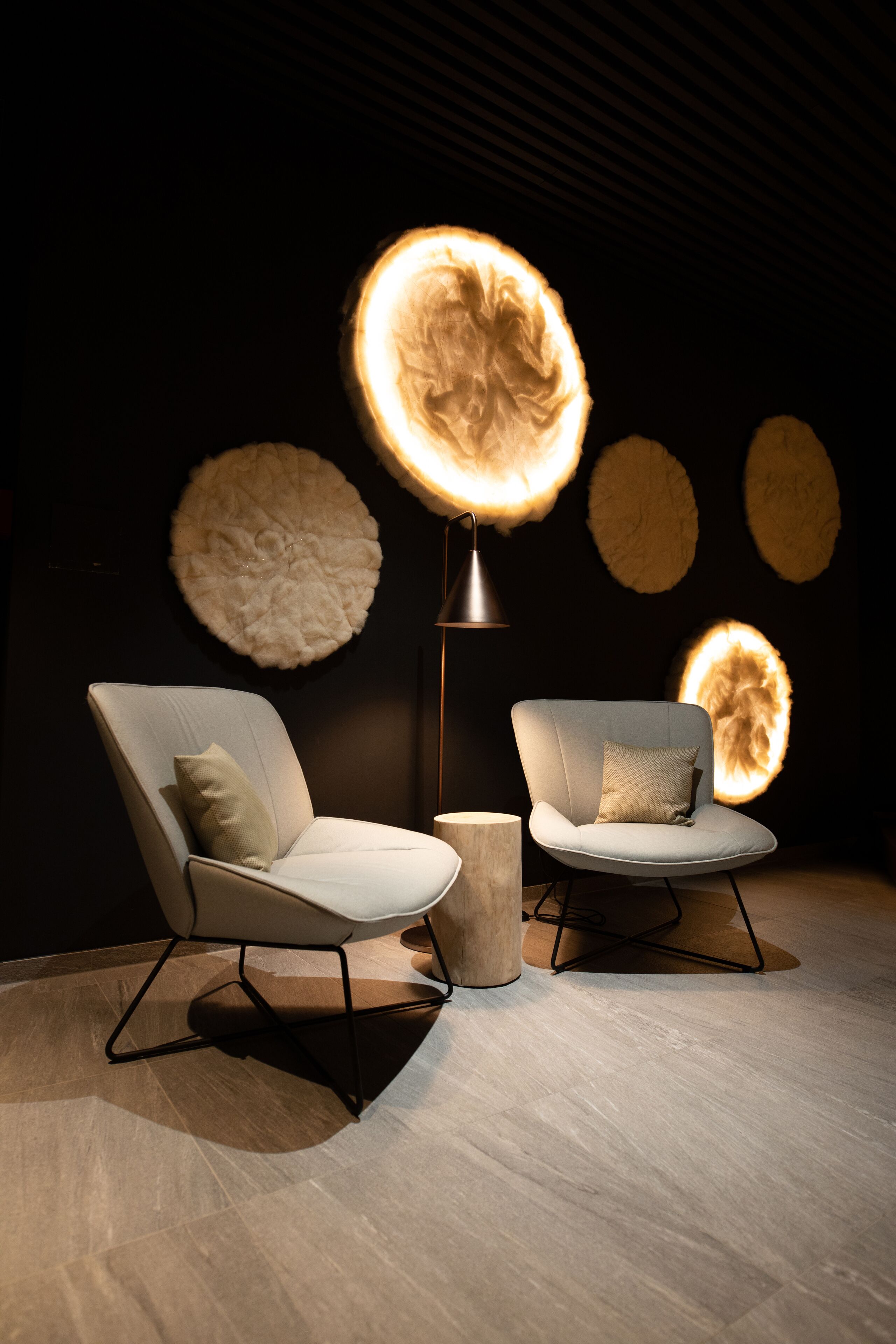 A modern interior with two white armchairs, a floor lamp, and wall-mounted circular light fixtures.