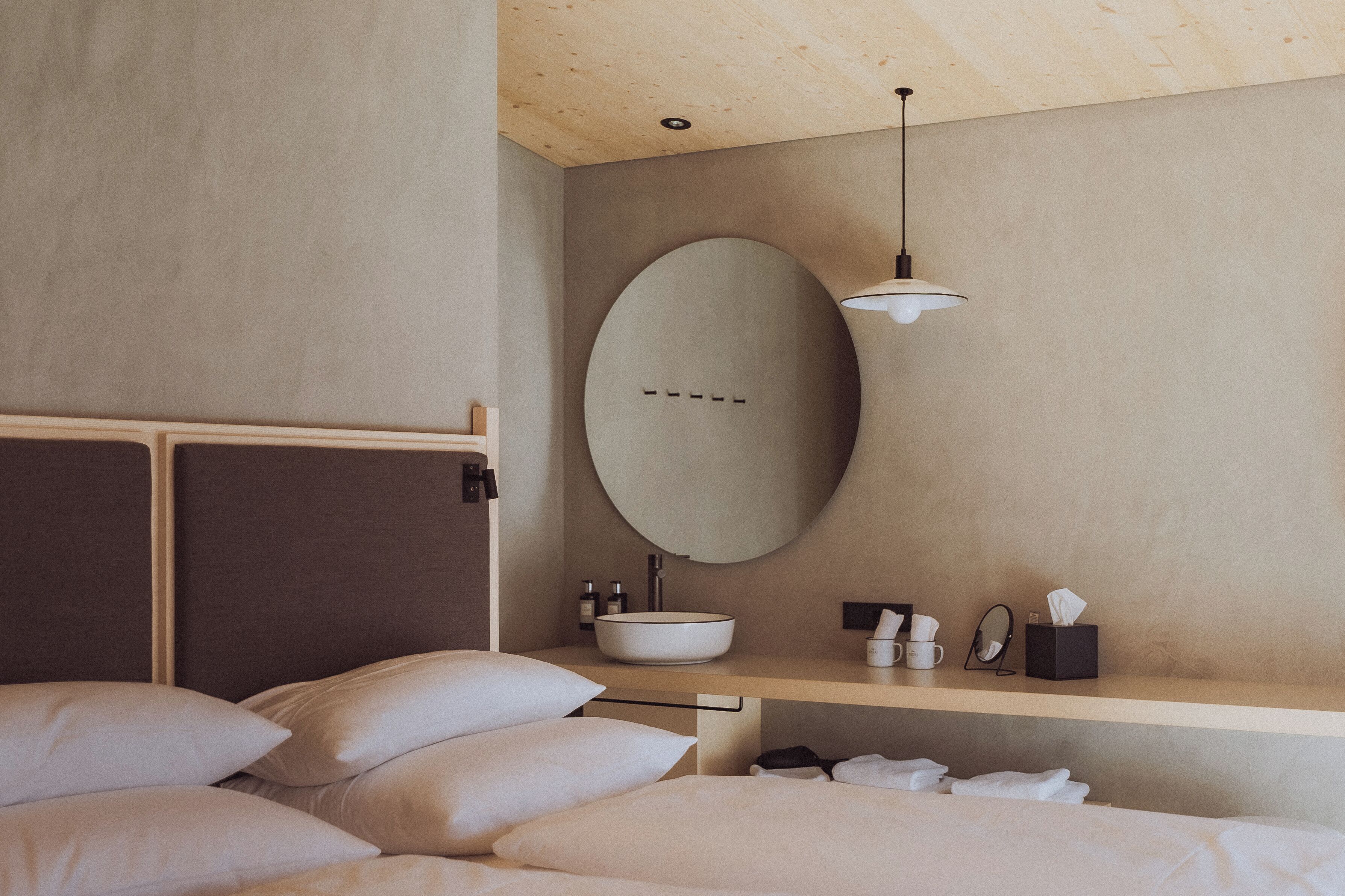 A modern bedroom with a large bed, a round mirror, a bedside table with toiletries, and a wooden headboard.