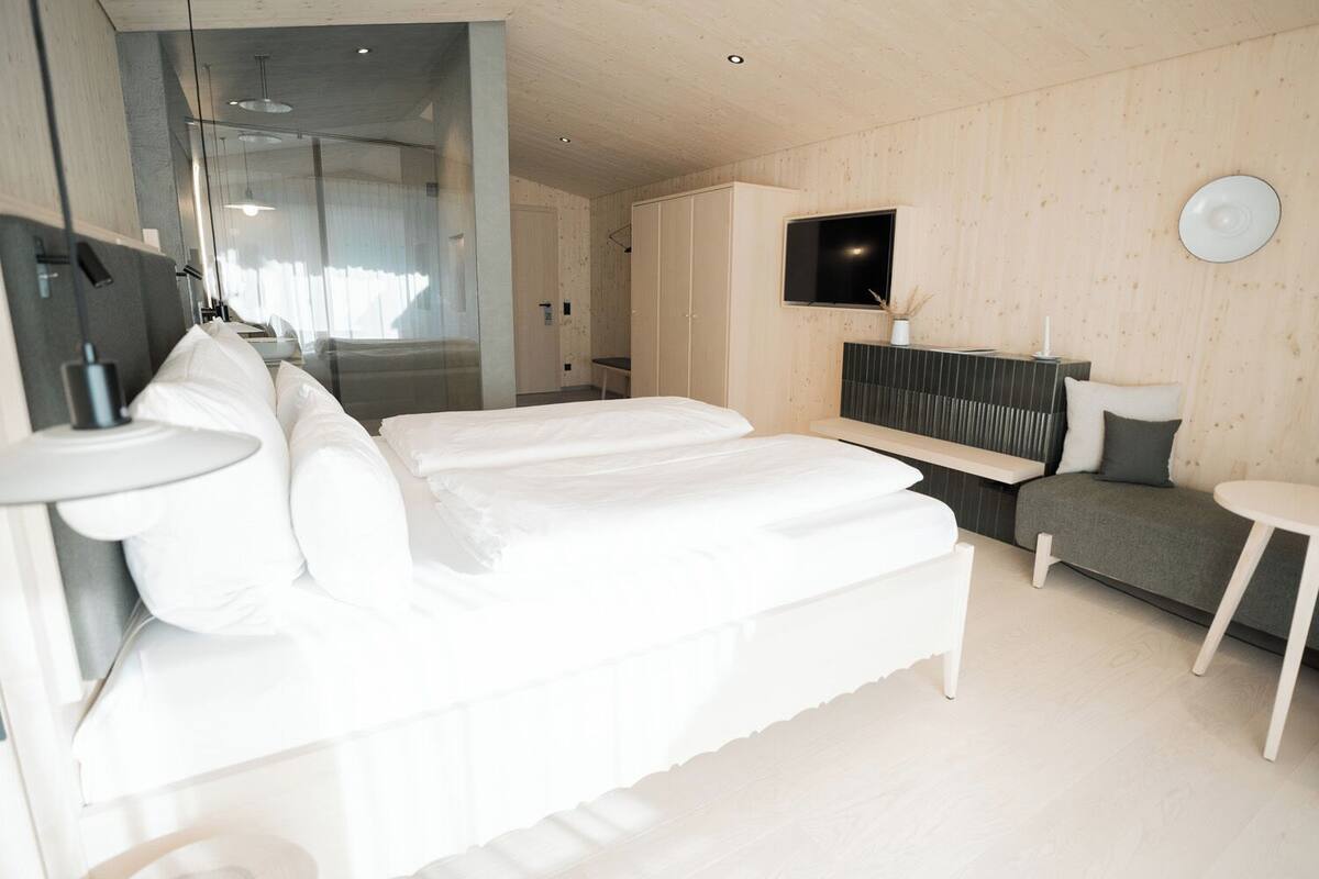 A modern bedroom with a large bed, a bedside table, a TV, and a small seating area.