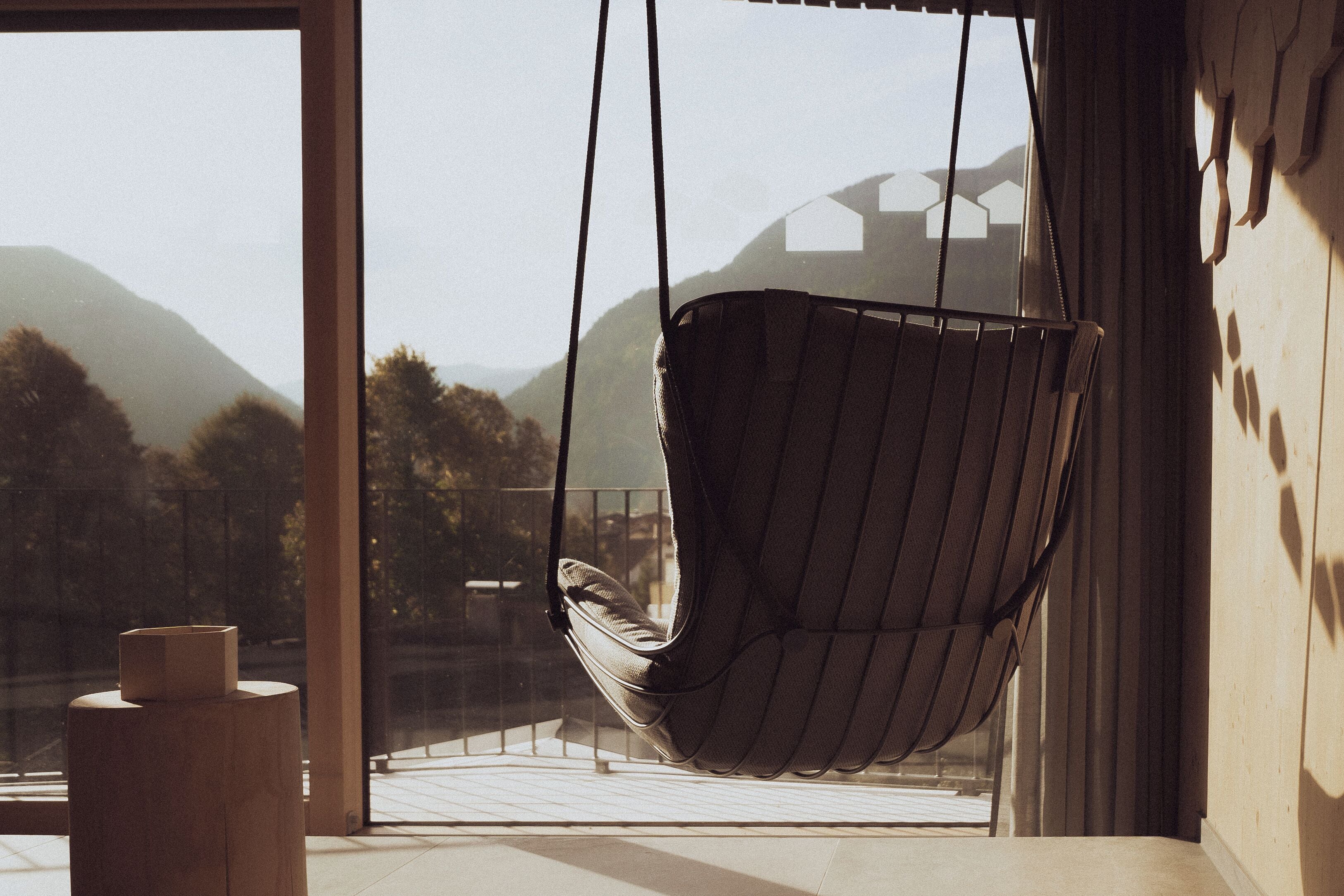 A hammock chair by a large window with a view of mountains and trees.