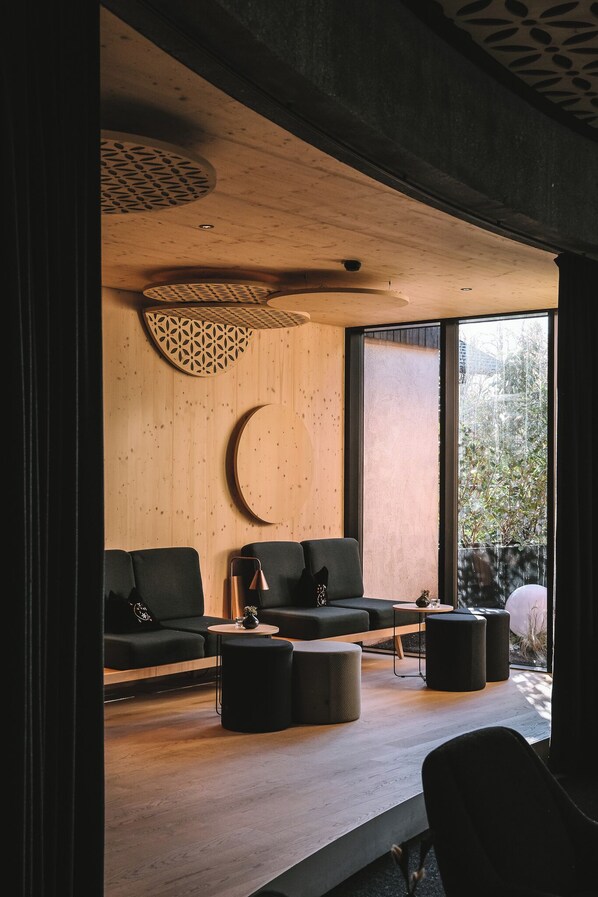 A modern interior with a wooden ceiling, a crescent moon wall decoration, and a large window offering a view of greenery. - Amrai Suites (Schruns)
