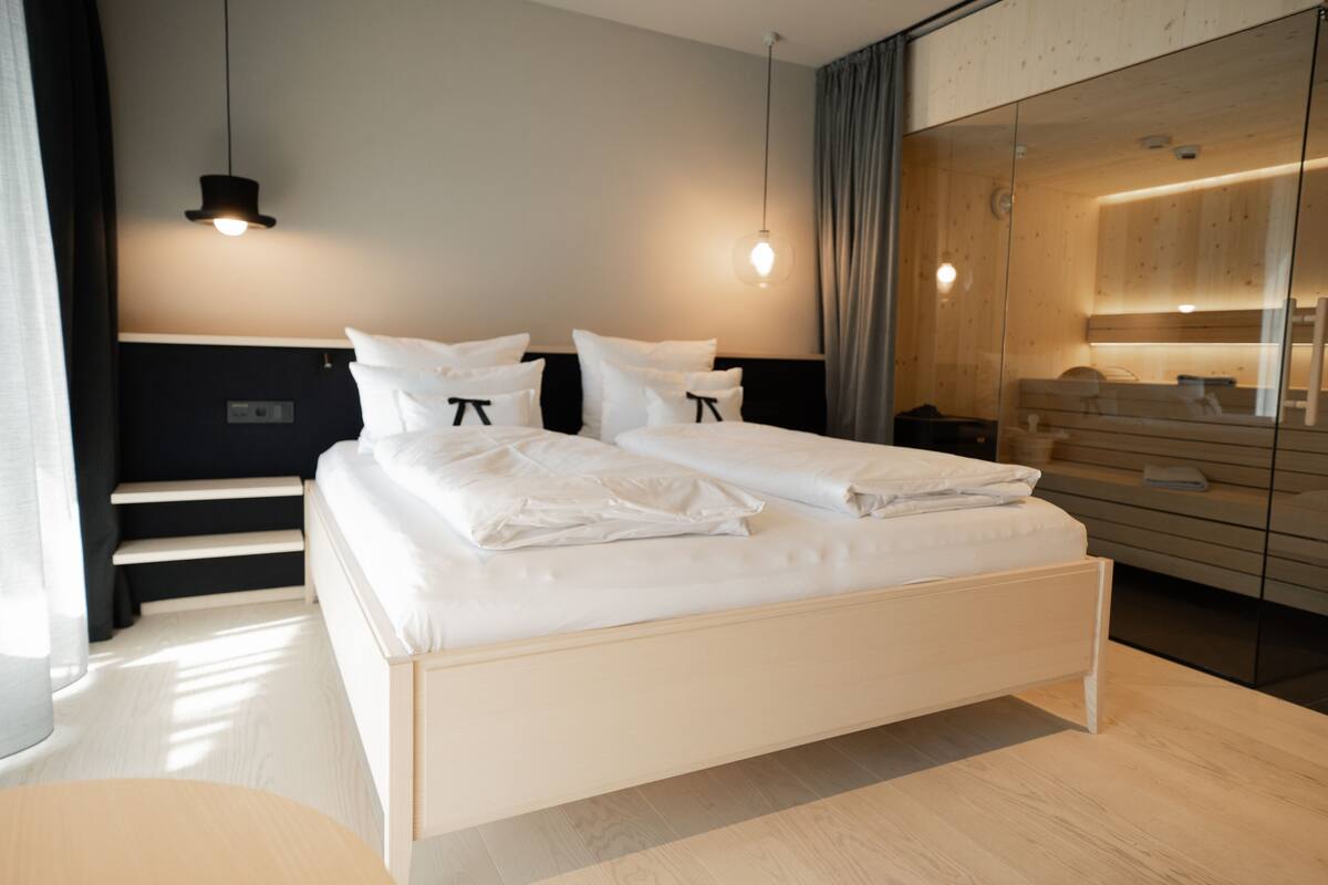 A modern hotel room with a large bed, bedside tables, a mirror, and a wardrobe.