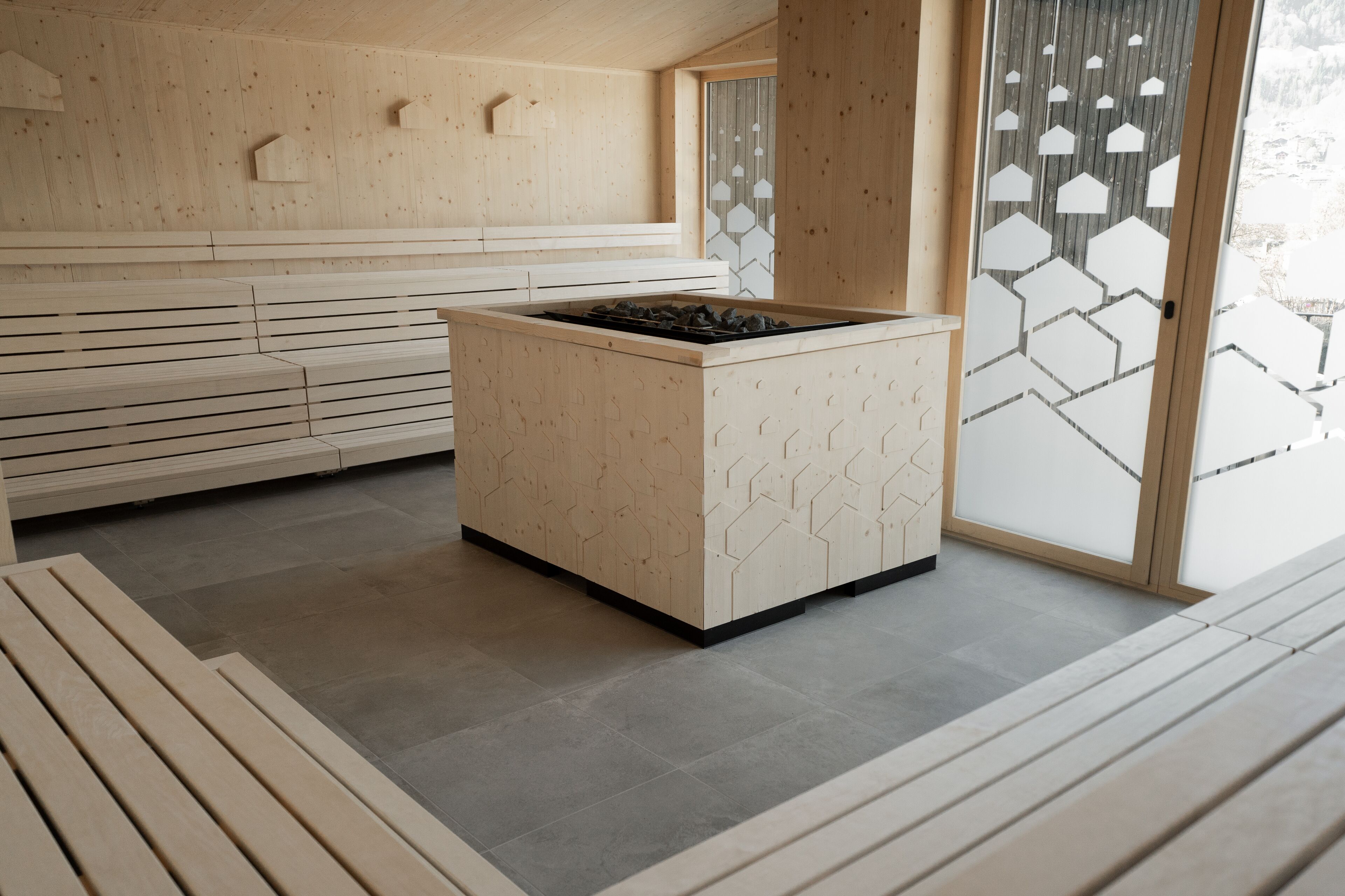 A modern interior with a central island stove, wooden benches, and a hexagonal patterned wall.