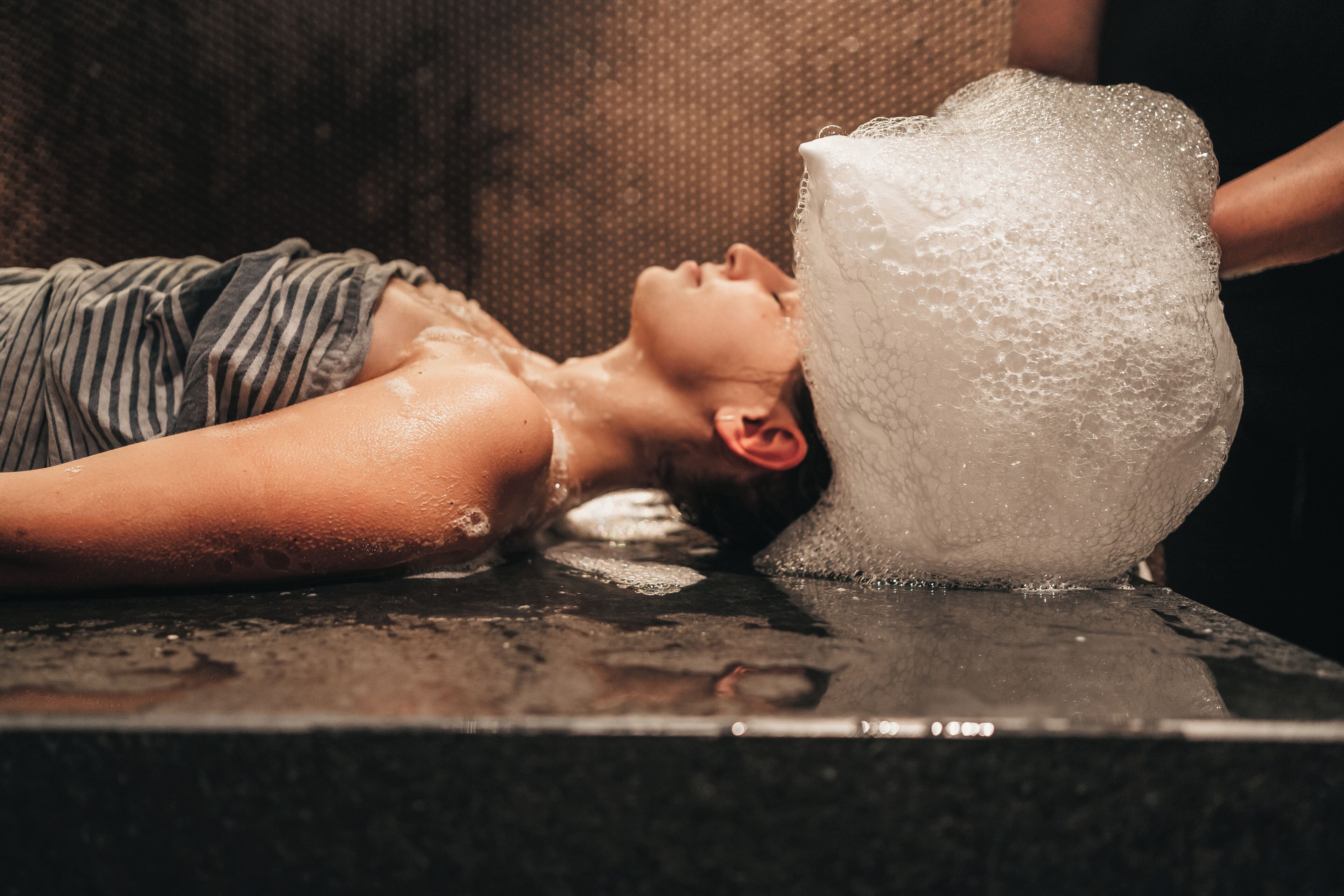 A person lying on a wet surface with a large bubble bath.