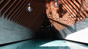 A modern interior with a sloped ceiling, a swimming pool, and hanging light fixtures. - Amrai Suites (Schruns)