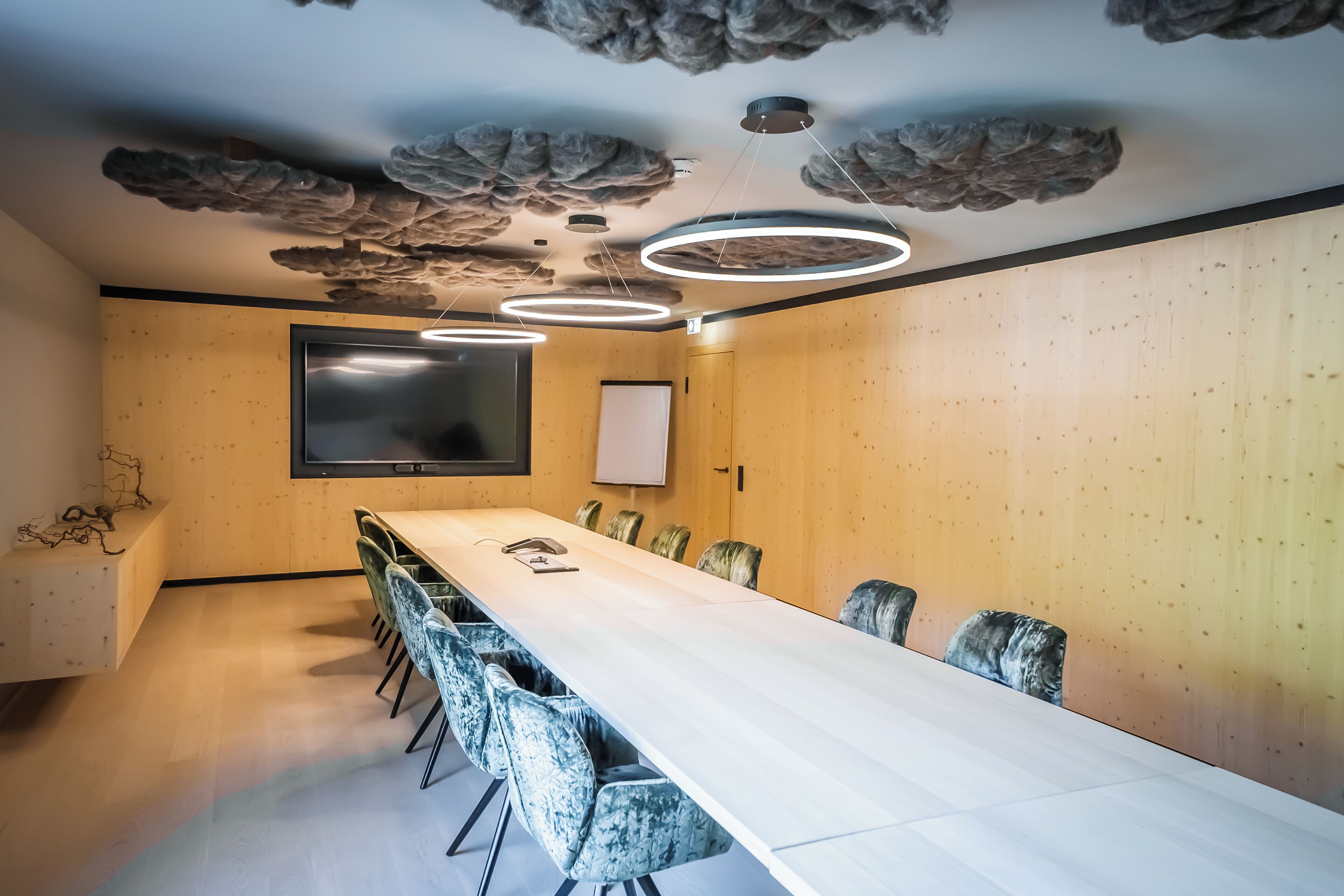 A conference room with a long table, chairs, a large screen, and modern lighting fixtures.