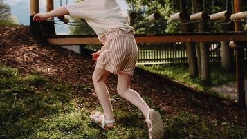 Eine Person in weißem Hemd und gestreifter Shorts schwingt auf einer Schaukel im Park.