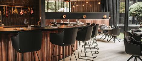A modern bar area with a wooden counter, black chairs, and pendant lighting.
