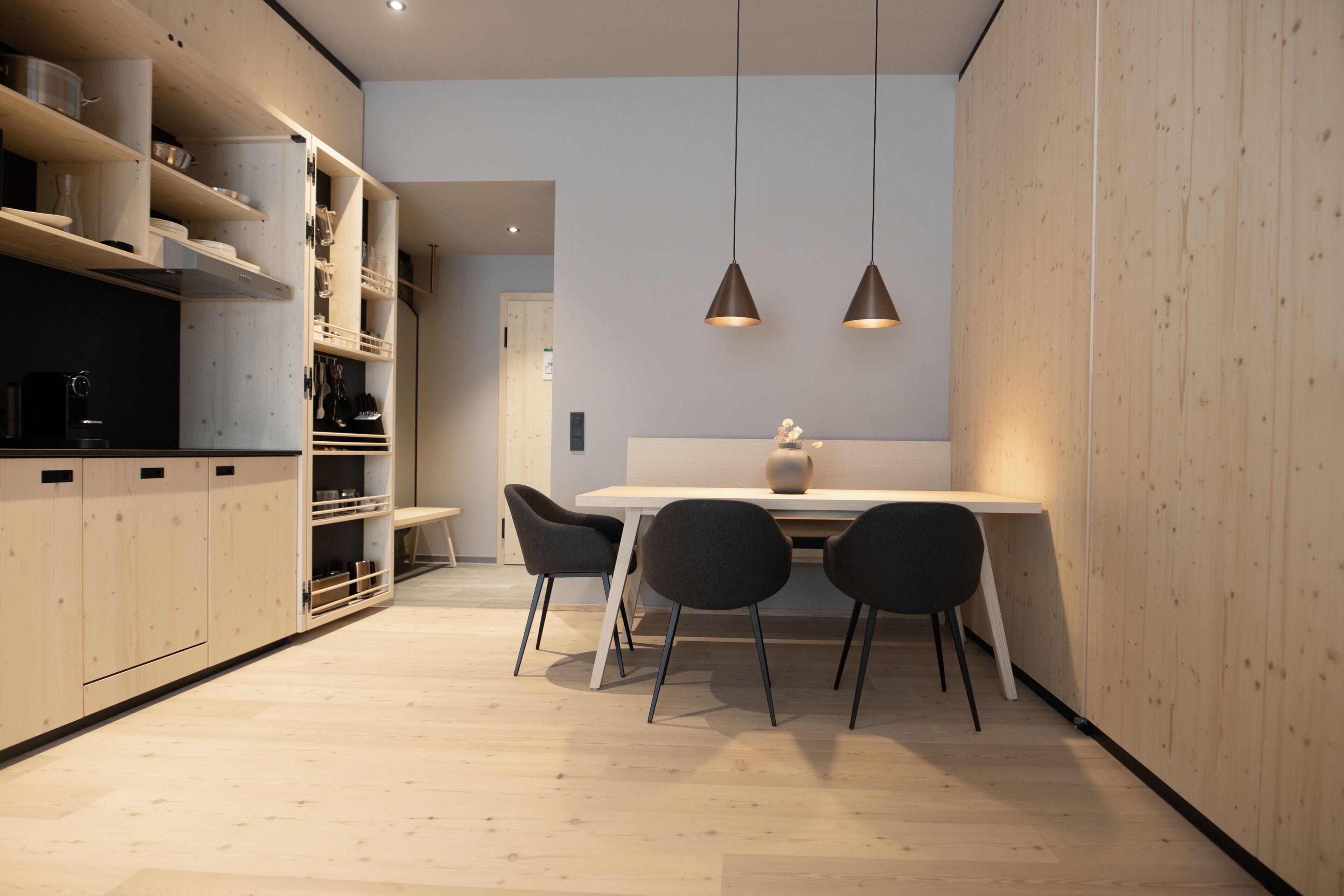 A modern kitchen with wooden cabinets, a dining table with chairs, and pendant lighting.