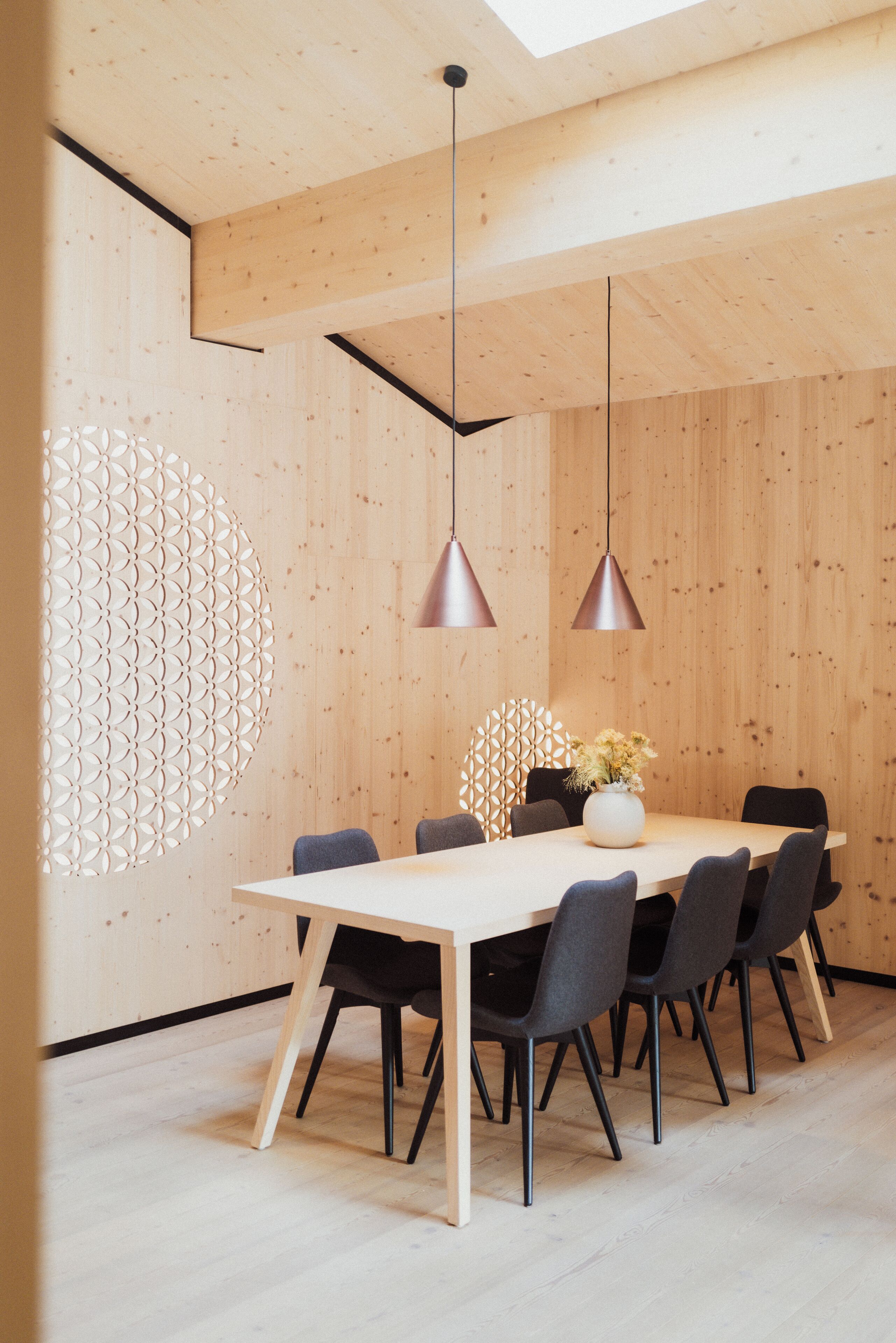 A modern dining area with a wooden table and chairs, pendant lights, and a decorative wall panel.