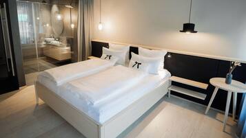 A modern hotel room with a large bed, a bedside table, a mirror, and a small round table with a vase.