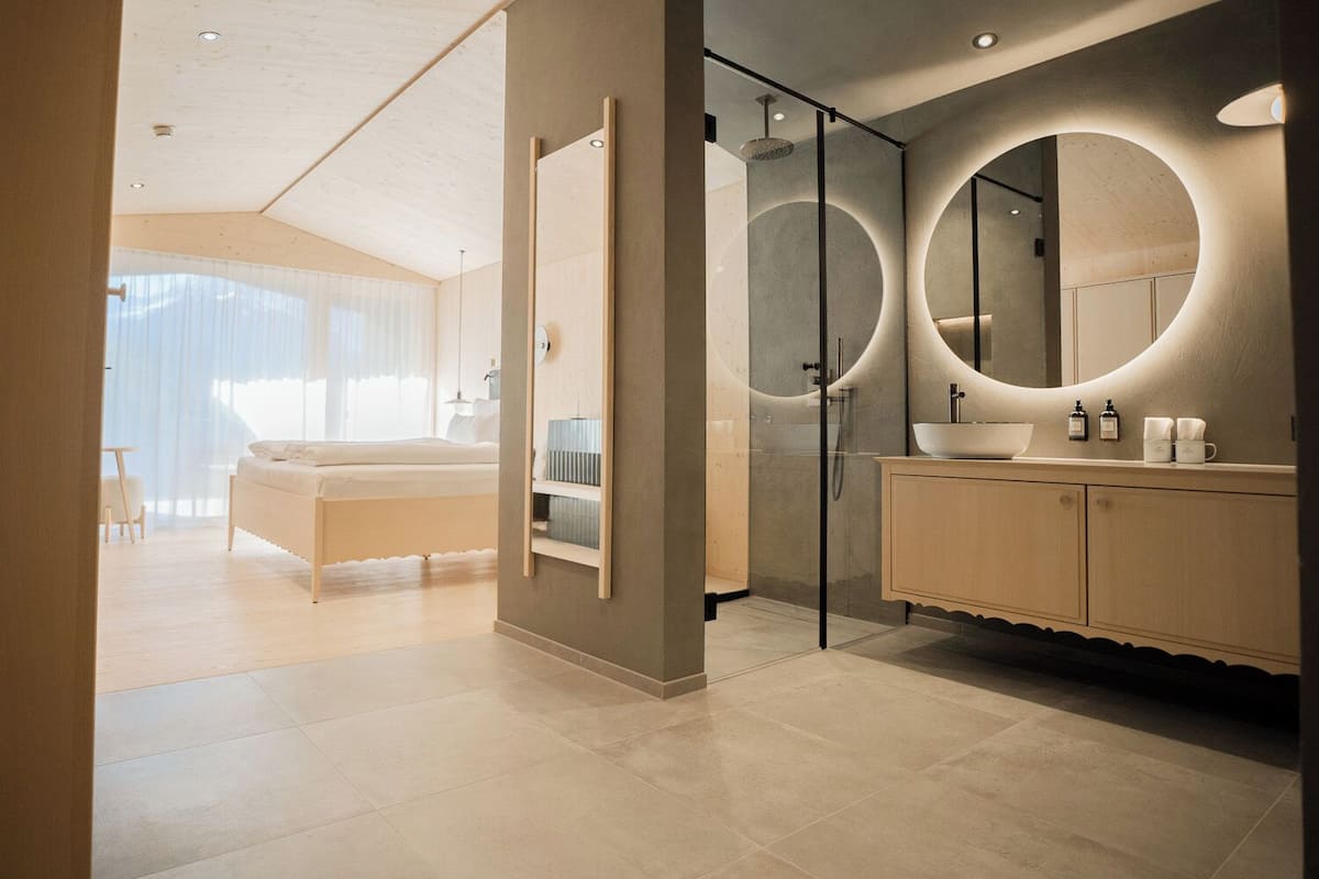 A modern bedroom with a large bed, a glass-enclosed shower, and a vanity with a mirror.
