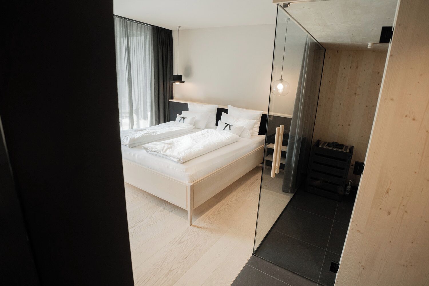 Een moderne slaapkamer met een groot bed, een glazen scheidingswand en een houten vloer.