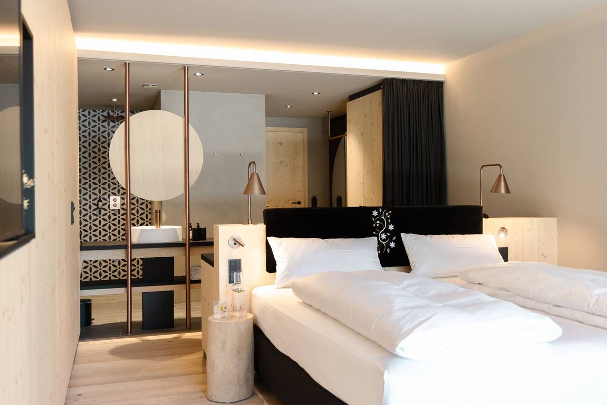 A modern bedroom with a large bed, bedside tables, a mirror, and a wooden cabinet.