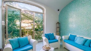 Ein Zimmer mit zwei weißen Sofas und Sesseln, einem kleinen Tisch mit einer Dekoration und einem großen Fenster mit Blick auf eine Berglandschaft.