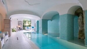 Ein Innenpool mit freiem Blick auf den Poolbereich, eine Sitzgruppe mit weißen Sofas und eine Steinwand an einer Seite.