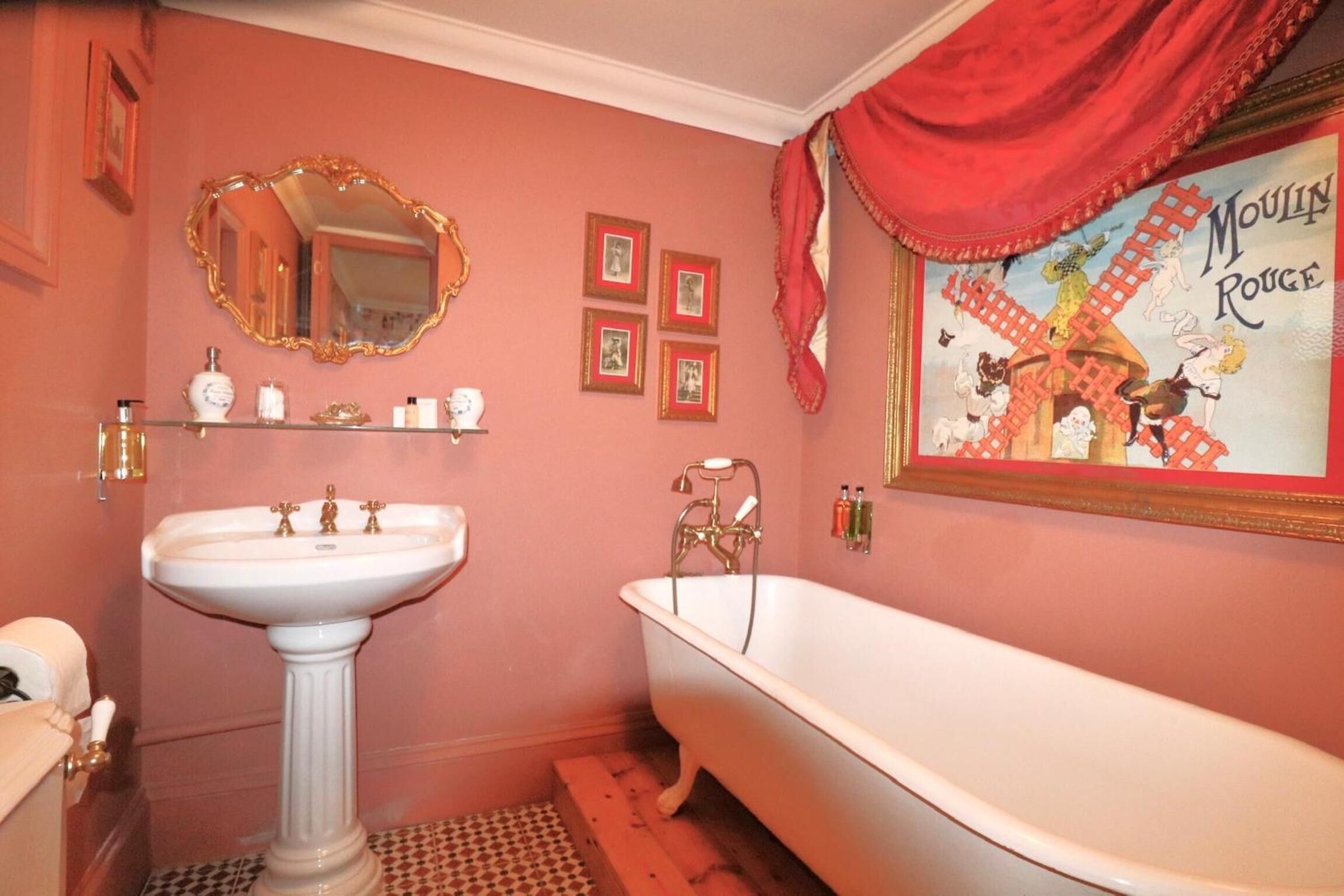 A bathroom with a pedestal sink, a clawfoot bathtub, a large mirror, and a Moulin Rouge poster on the wall.
