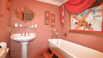 A bathroom with a pedestal sink, a clawfoot bathtub, a large mirror, and a Moulin Rouge poster on the wall.