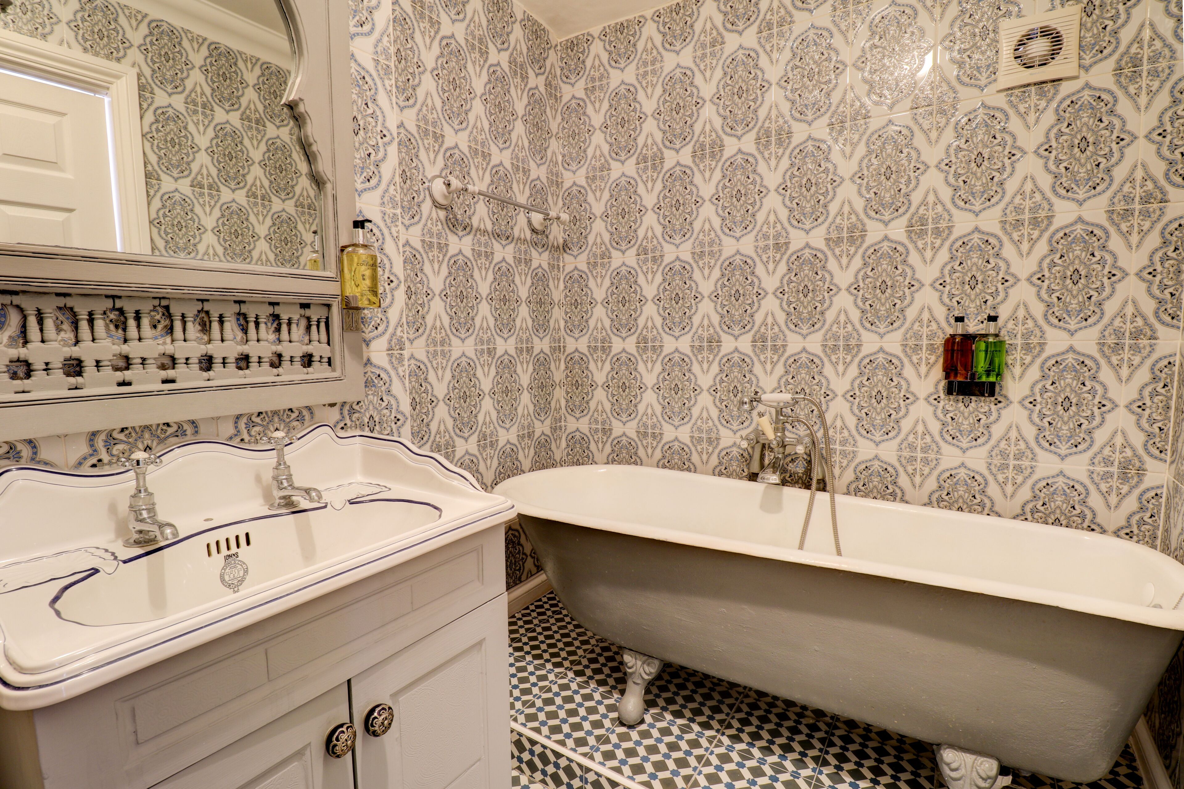 Un bagno con una vasca da bagno d'epoca, un lavabo con maniglie decorate e piastrelle a motivi.