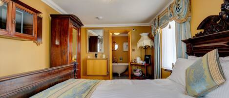 A bedroom with a large bed, wooden headboard, a bedside table with a lamp, and a mirror.